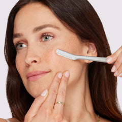 Woman using Tweezerman facial razor for women to gently remove peach fuzz and smooth cheek skin