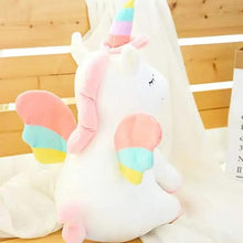 White unicorn plush with rainbow horn and striped mane, embroidered eyes, sitting on bed