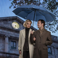 Couple using UV protection travel umbrella in the rain outside a historic building at dusk