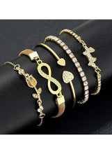 Stacked gold crystal charm bracelets with cross, heart, and studded tennis-style bands