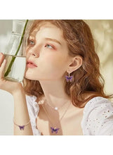 Purple butterfly pendant necklace and purple drop earrings on a model