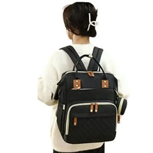 Black baby changing backpack worn on back with quilted front panel and tan leather-look straps