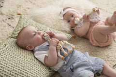 Two babies lying on rug holding and chewing Sophie La Girafe teether UAE natural rubber teether