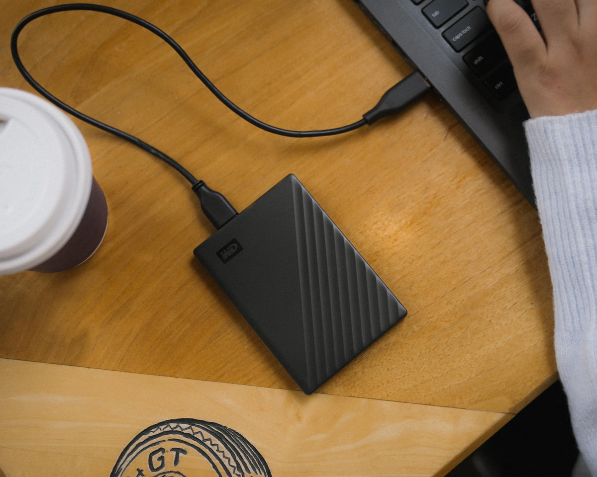 Western Digital portable hard drive for laptop connected to laptop on wooden desk next to coffee cup