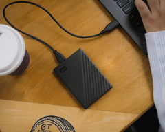 Western Digital portable hard drive for laptop connected to laptop on wooden desk next to coffee cup