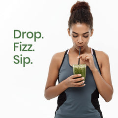 Woman in workout tank sipping green smoothie through straw next to visible text promoting wholefood multivitamin with superfoods