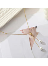 Gold lariat necklace with twin pearl drops worn over a white shirt