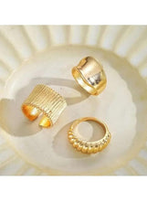 Gold-tone ring set with textured open bands and a wide cuff, arranged on a light tray