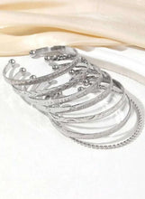 Silver-tone open cuff bangles laid on fabric, mixed textures and small studs