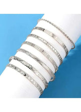 Close-up of silver-tone open cuff bangles with textured bands and beaded accents