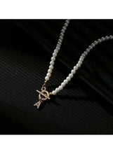 White pearl necklace with gold initial charm and loop clasp, close-up