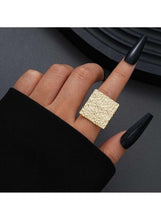 Gold textured square ring worn on finger, raised geometric surface
