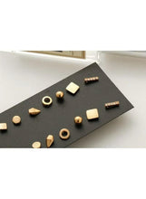 Gold stud earrings set with round, square, and bar shapes on black card