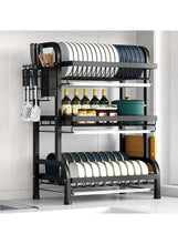 Black dish drying rack with drain board and utensil holder, holding plates on two levels