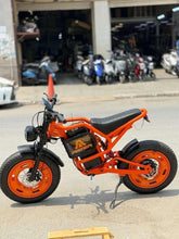 Orange electric bike with black seat and front headlight parked outdoors.