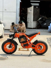 Orange electric bike parked on street with black seat and fat tires.