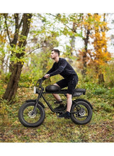 Electric fat-tire bike ridden outdoors, with wide tires, front headlight, and rear rack.