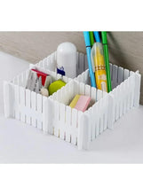 White expandable drawer organizer separator forming sections for pens and small supplies.