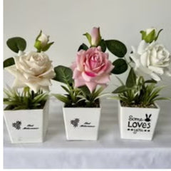Three artificial flowers in white pots including a pink rose and artificial purple rose plant by Huitich