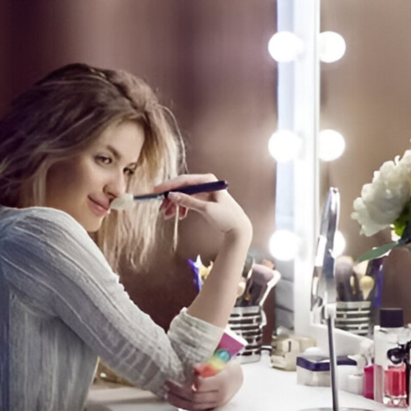 Woman holding Huitich rainbow lip gloss applying makeup at vanity mirror with lights