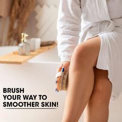 Woman in white robe using wooden bath brush with massage beads to exfoliate her leg skin