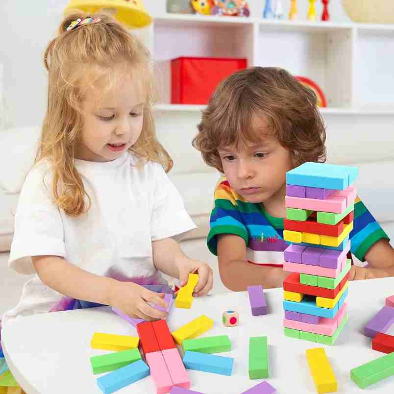 Two kids playing with colorful wooden building blocks for kids on a white table indoors