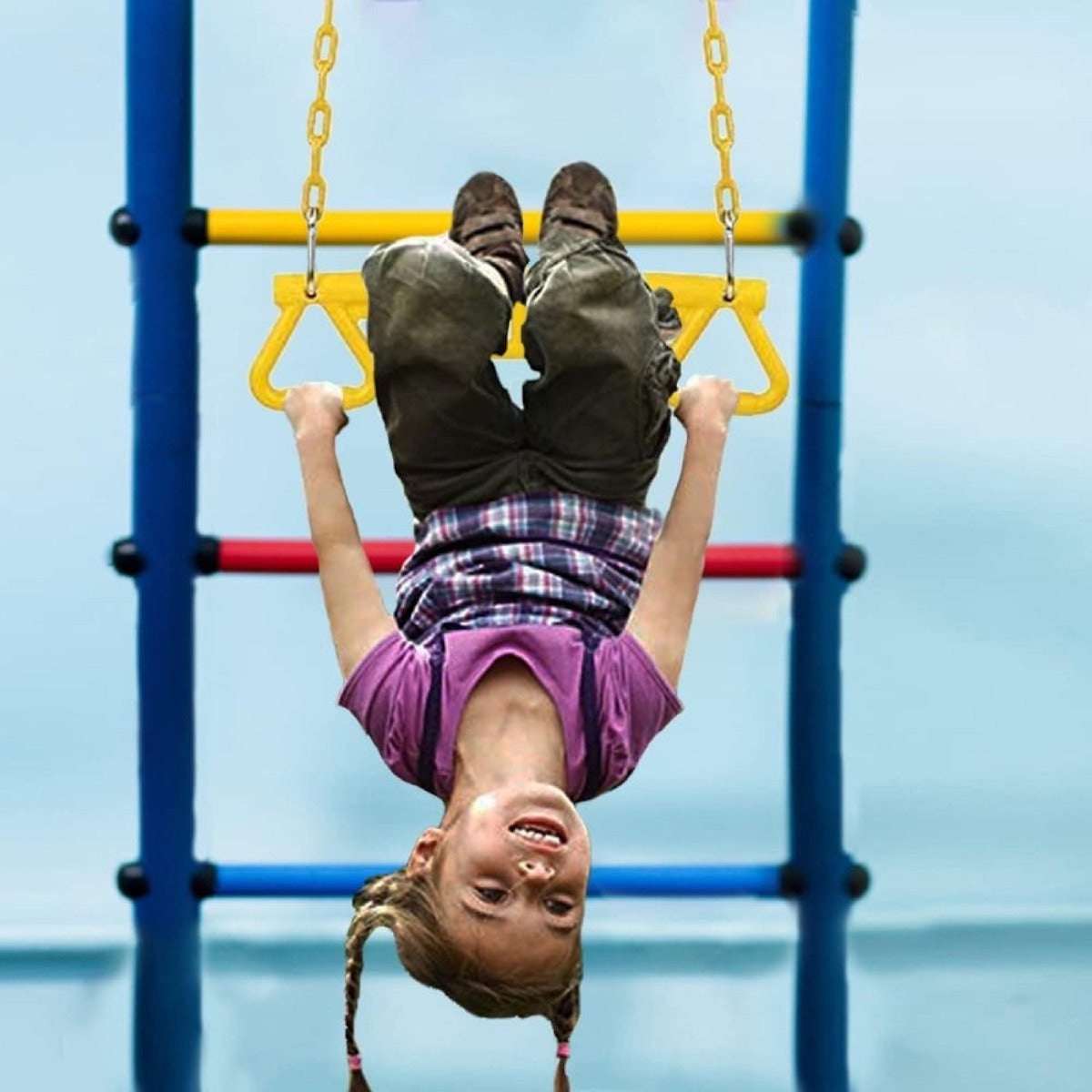 Child playing on yellow park gym ring bar, hanging upside down on colorful playground equipment